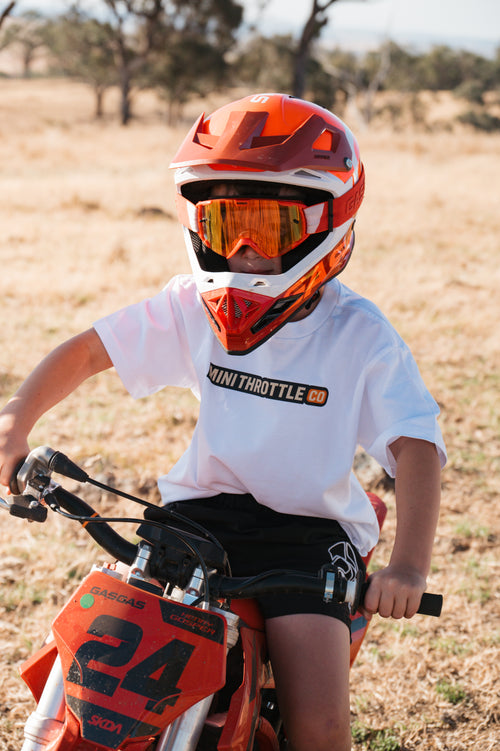 Child wearing motocross gear on a dirt bike in an outdoor setting