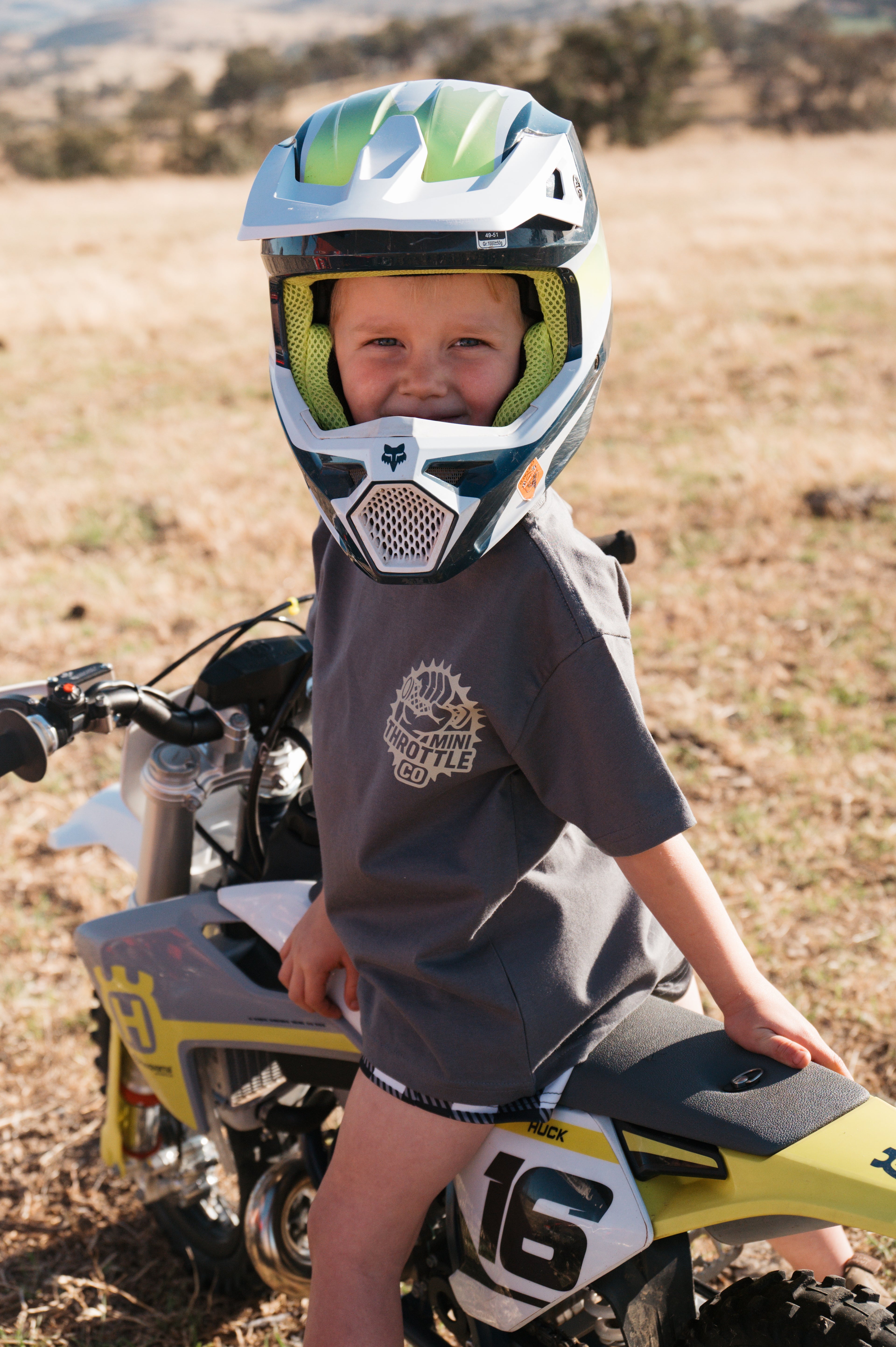 Child wearing a helmet and sitting on a dirt bike in an outdoor setting
